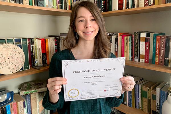 Jordan Woodward, Winner of 2020-2021 WAC Award, holding her award certificate in front of a bookshelf