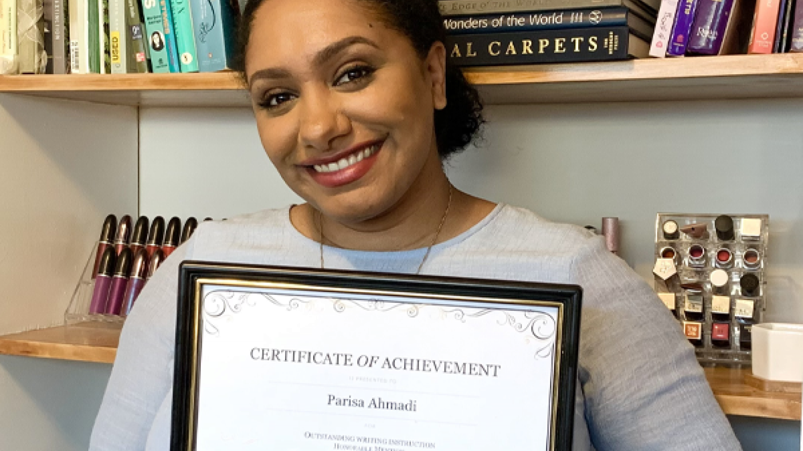 Parisa Ahmadi, honorable mention for the 2020-2021 WAC Outstanding Writing Instruction Award, holding her award certificate in front of bookshelves